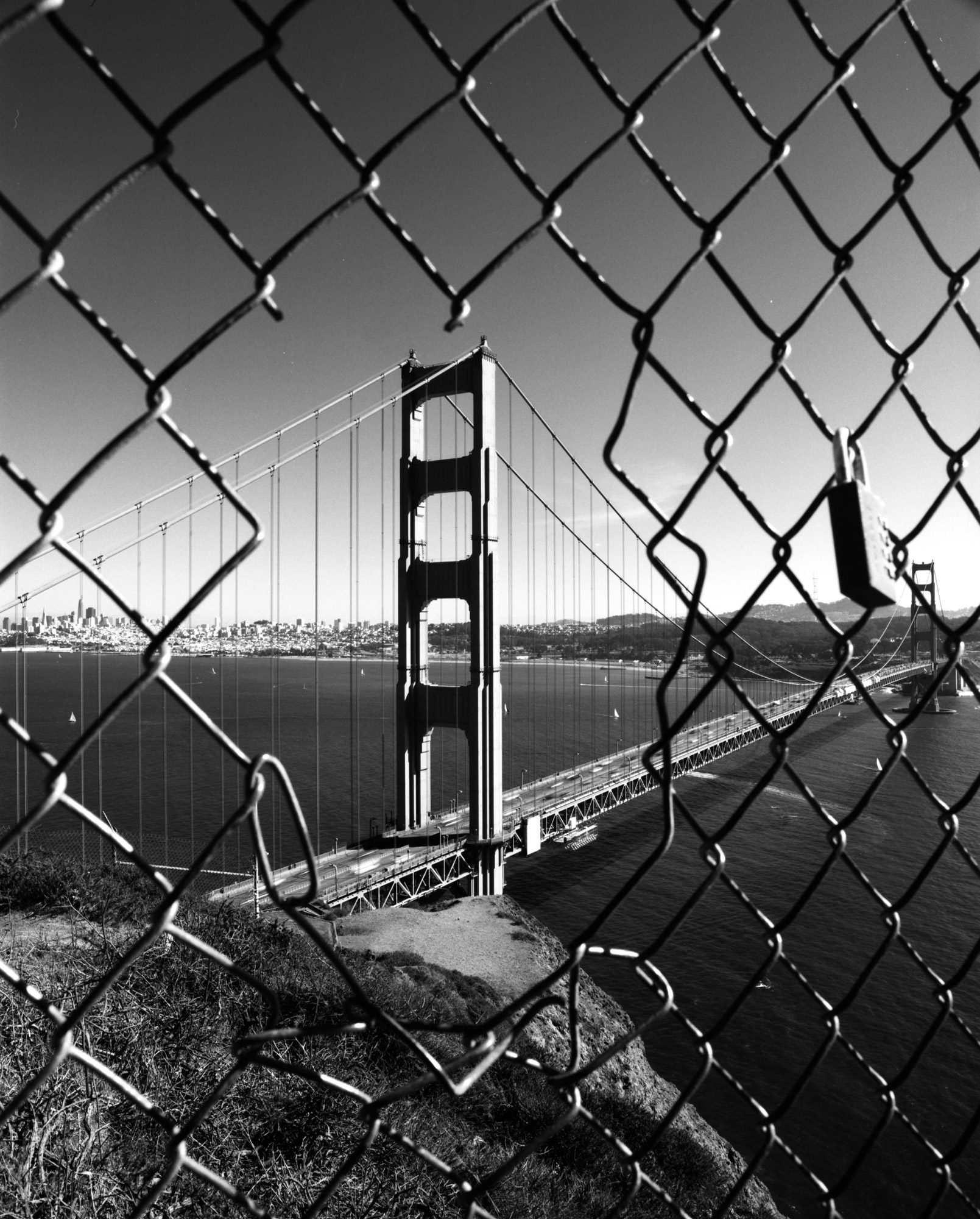 Golden gate bridge, framed through a gap in a wire fence. Shot on ILFORD Delta 100 black and white film by Sergio Lopez