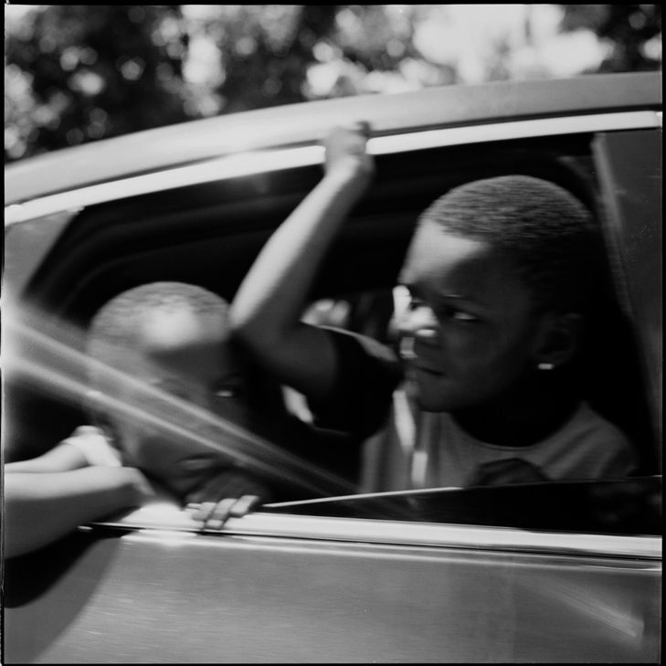 wo children look out the window as they drive by a protest, Salt Lake City, UT. Ilford Ortho Plus.