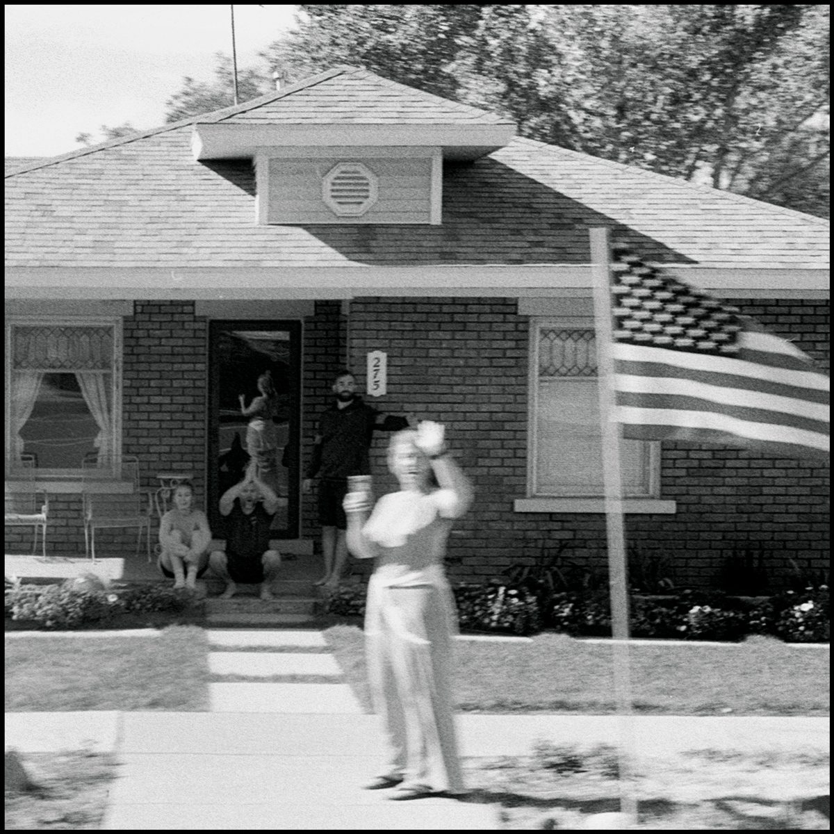 A family stands outside their home and watches a Pro Trump parade drive by. Hurricane, UT. Ilford Delta 400.