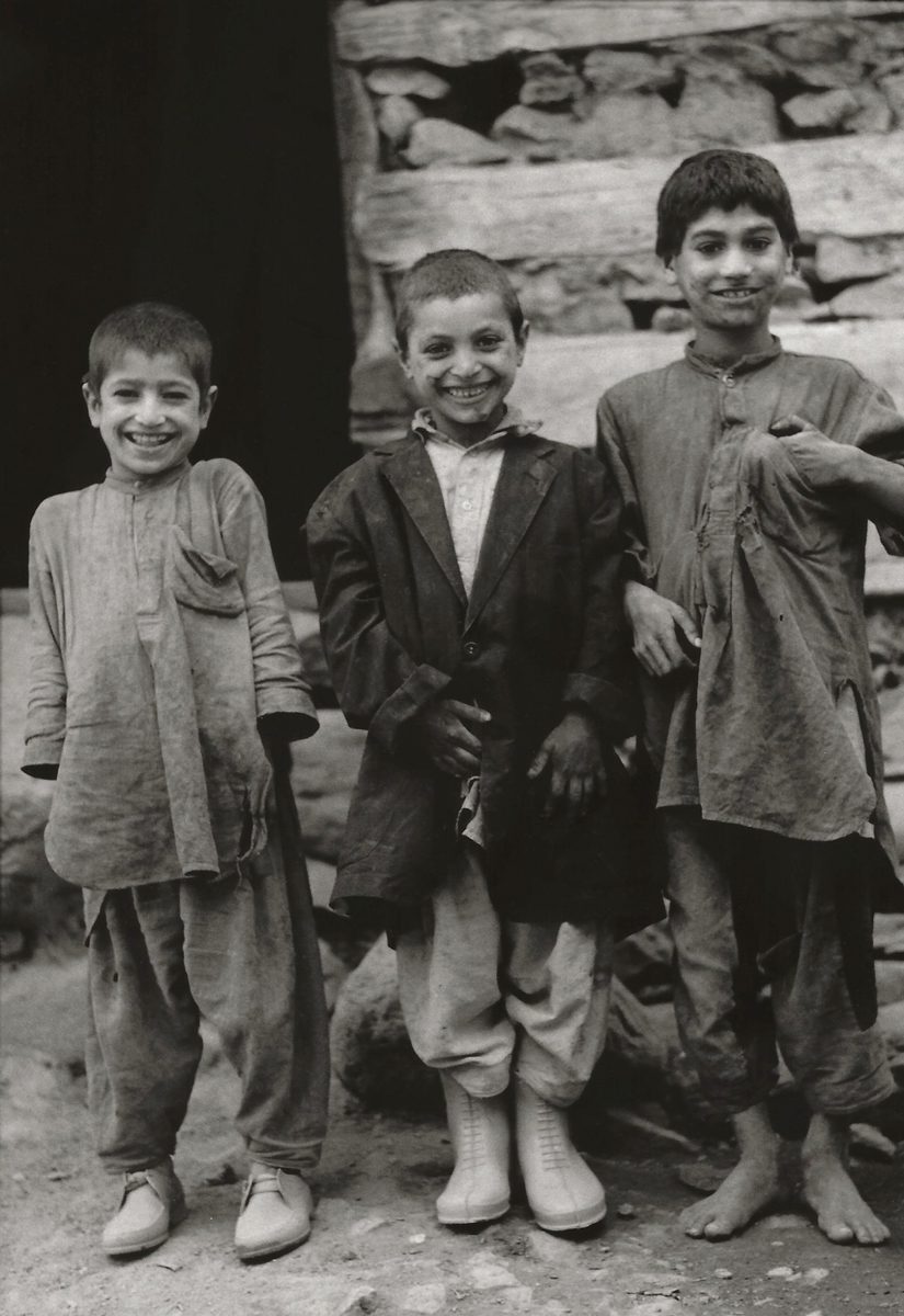 Black and white photograph of three children stood in a line smiling at the camera
