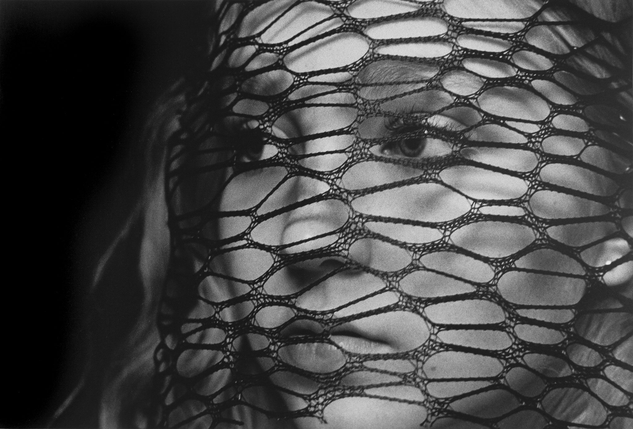 Black and white darkroom print of a woman's face with a lace netting covering it and creating a pattern
