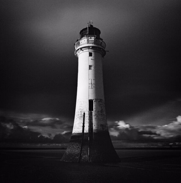 Black and white lighthouse looking over a rocky sea, and soft clouds in the background shot for How I got this picture series on ILFORD Photo website by - David Jones