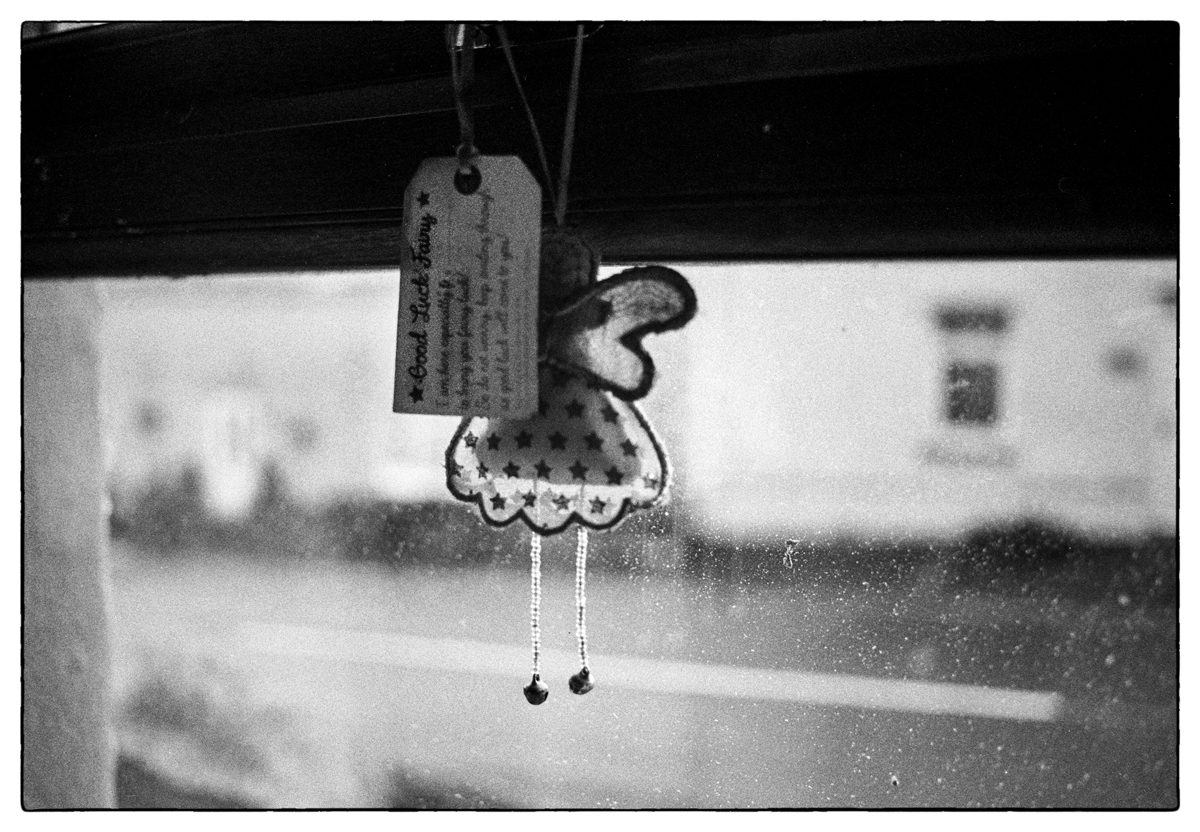 Black and white photograph of a fairy car key chain hung up on the dashboard of a car.