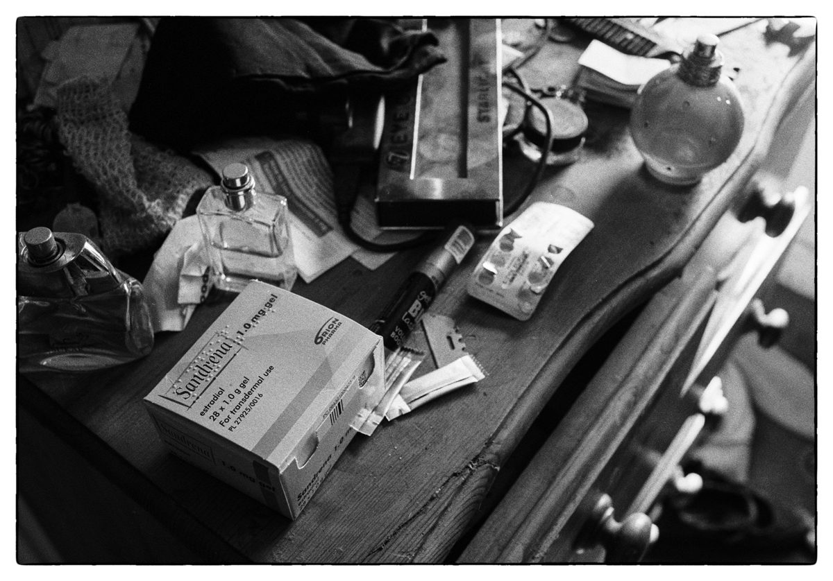 Black and white photograph of knick-knacks displayed on top of drawers, including tbalets and perfume bottlesincluding