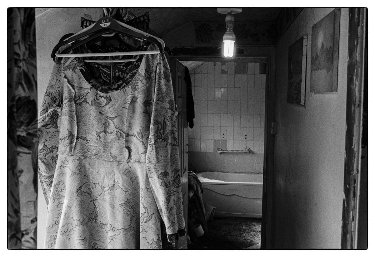 Black and white photograph of a dress hung up on a railing, with the view of a bathroom in the background