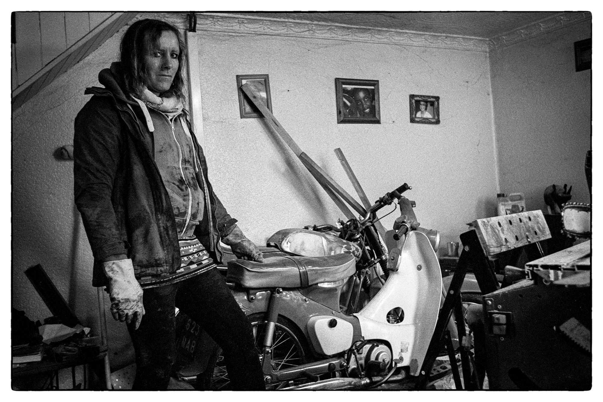 Black and white photograph of a transgender woman stood next to a motorbike indoors