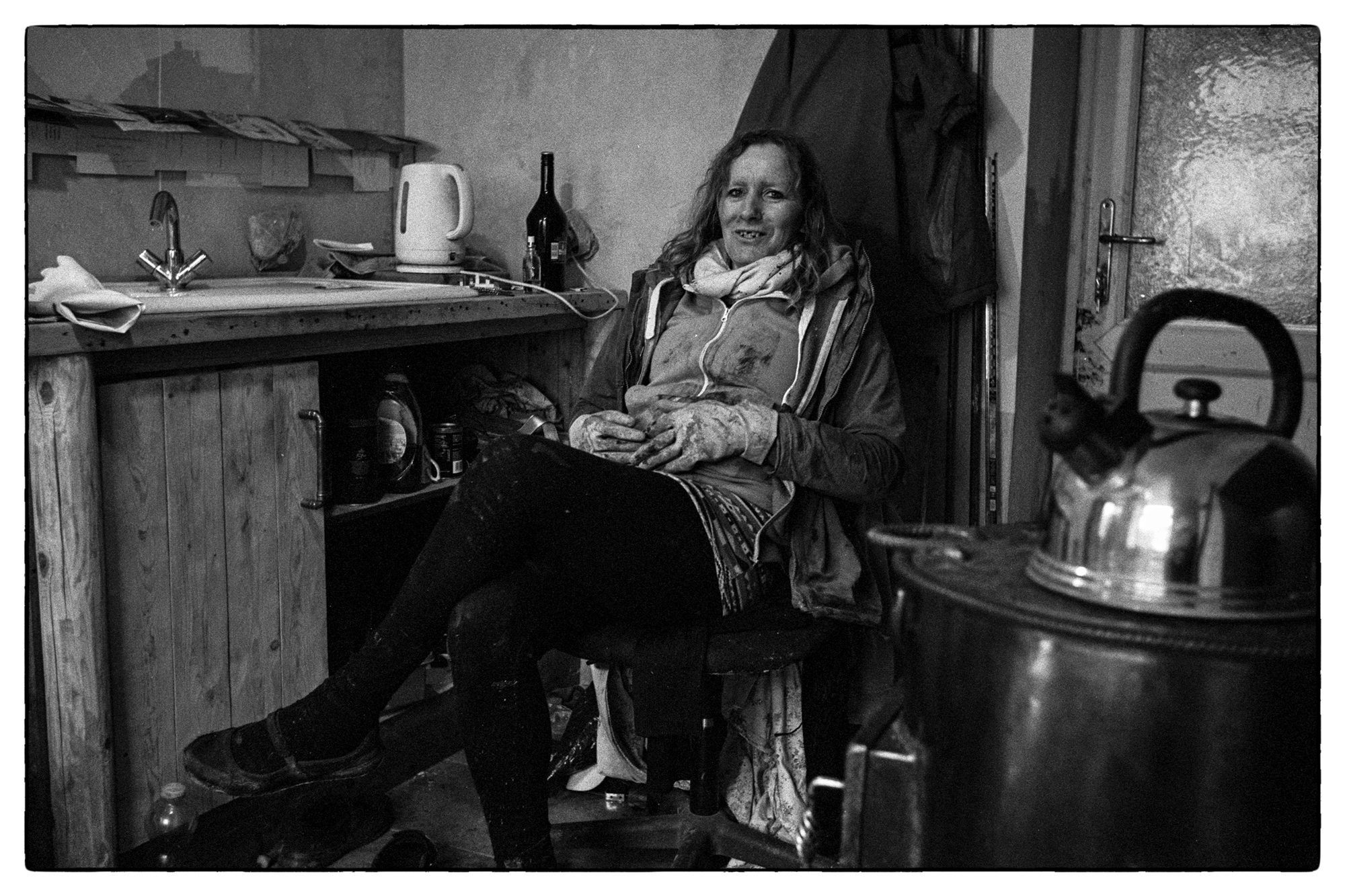 Black and white portrait photograph of a transgender woman sat down on a chair with her legs crossed