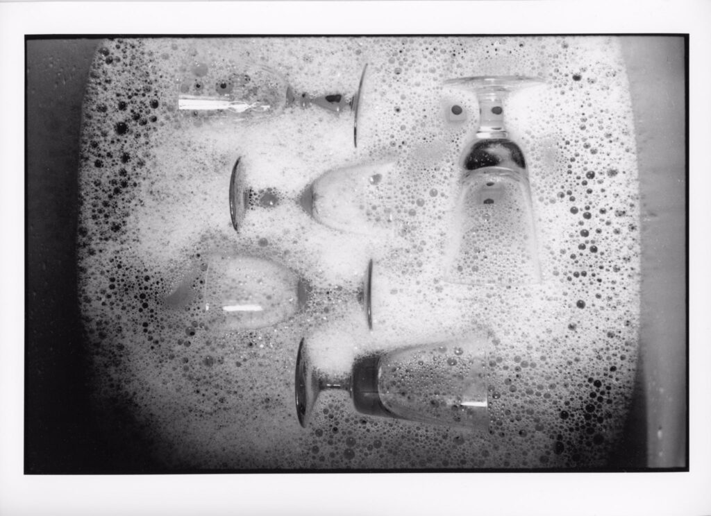 Black and white photograph of glasses laying in a bowl of soap