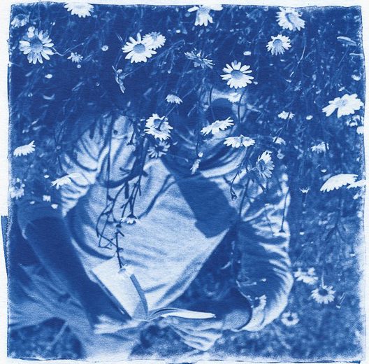 Blue cyanotype of man laying down with his face being covered by flowers