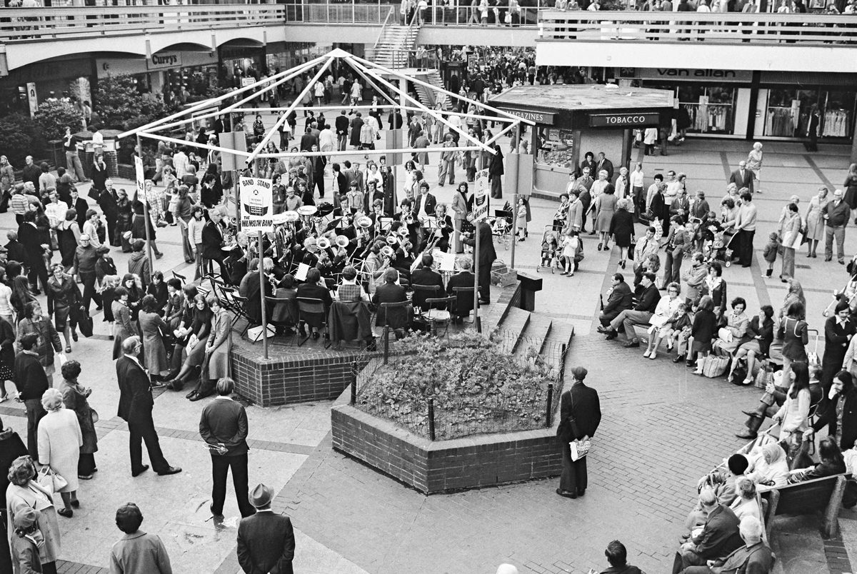 Black and white photo of a band playing in the centre of a town with a crowd surrounding them