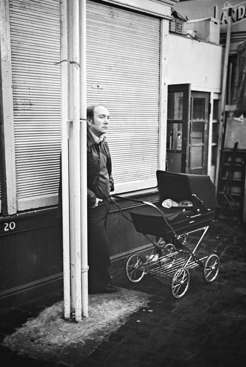 Black and white photo of a man holding a push chair with a baby inside
