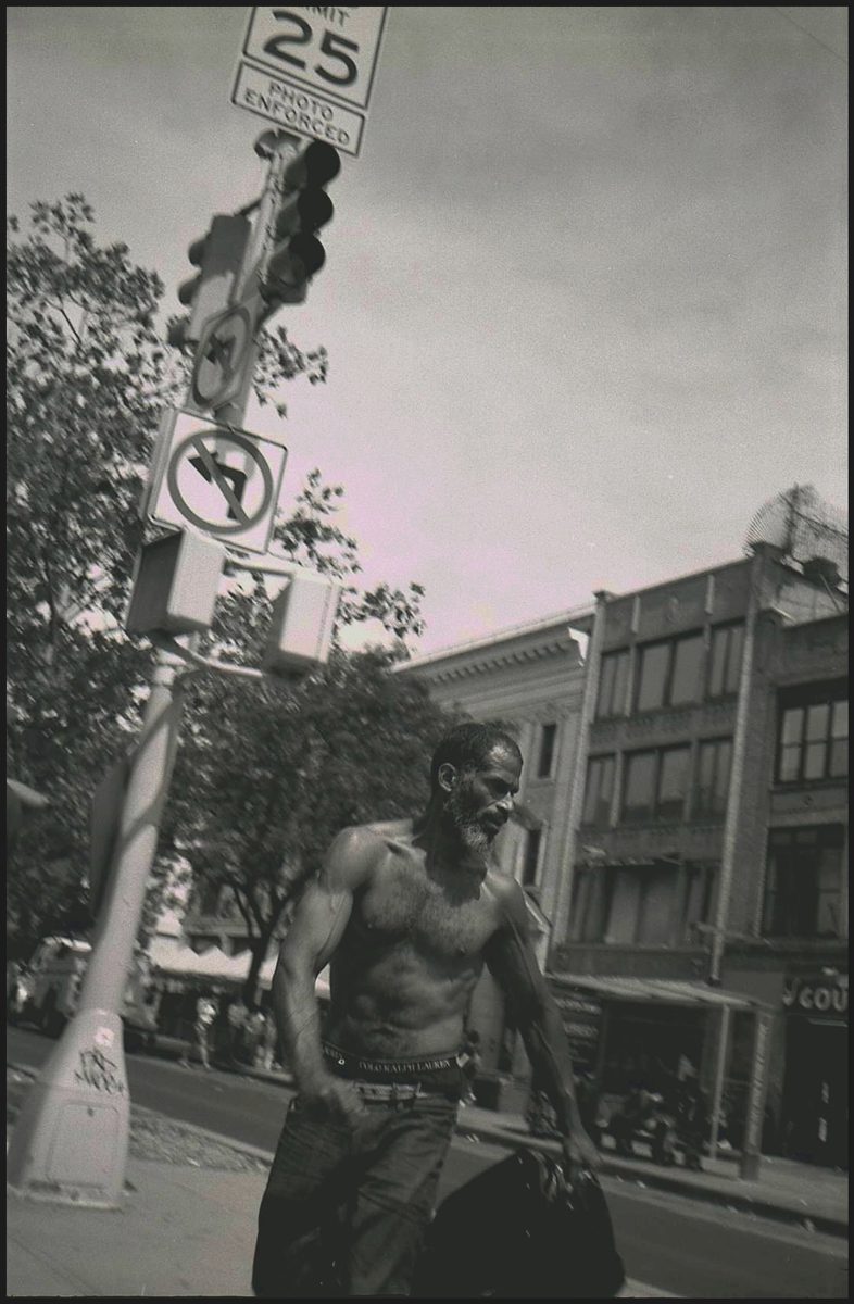 Black and white photo of a topless man walking down the street