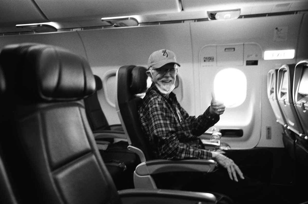 Black and white photo of a elderly man sat on a airplane waving