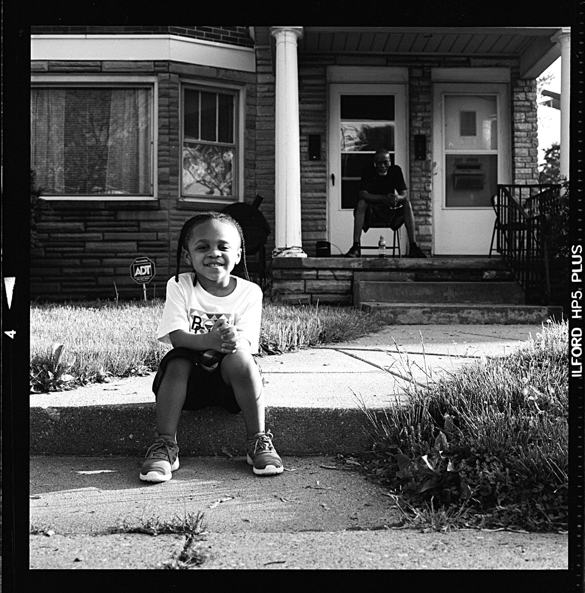 Black and white photo of a little girl sat down with her grandfather sat in the background