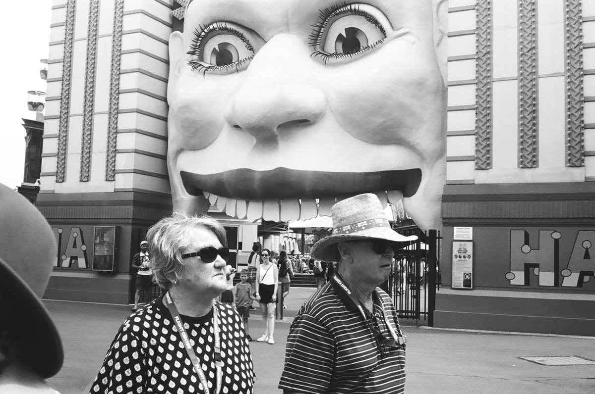 Black and white image of two people walking past a shop with a face as the door