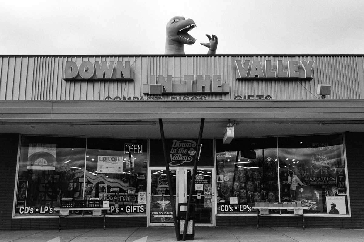 Black and white photo of a shop with blow up dino coming out at the top