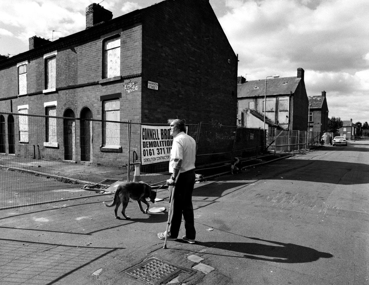 Black and white photo of a man stood in the street with his dog