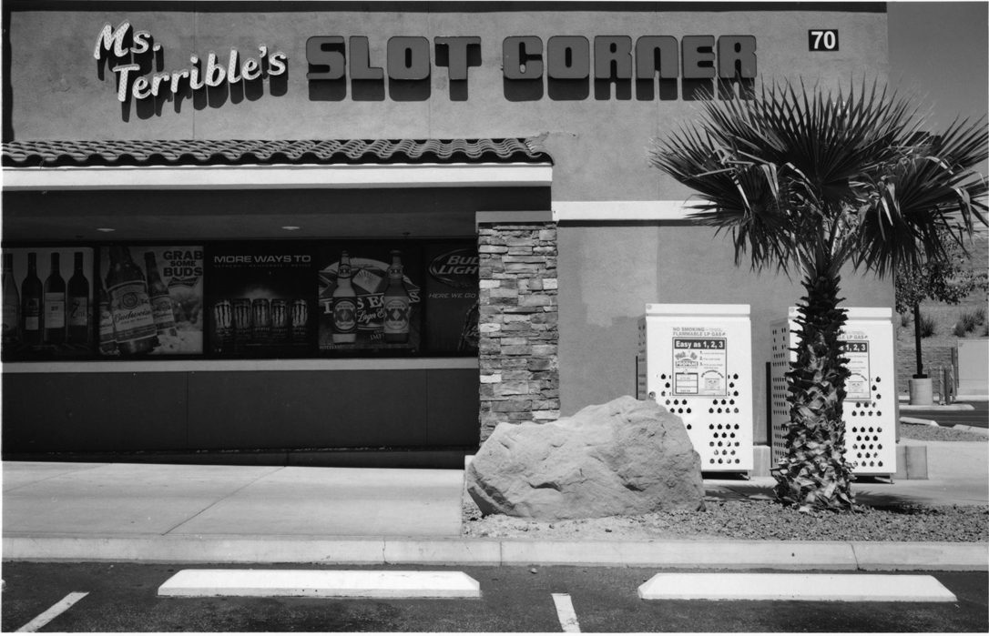 Black and white image of the front of a shop with a tree