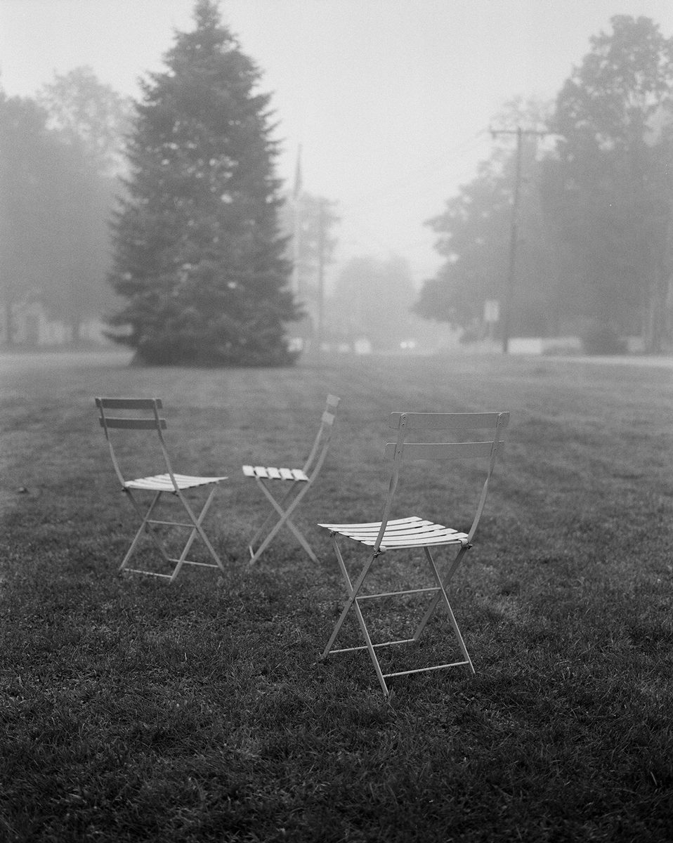 Black and white photo of outdoor chairs with a table in a garden