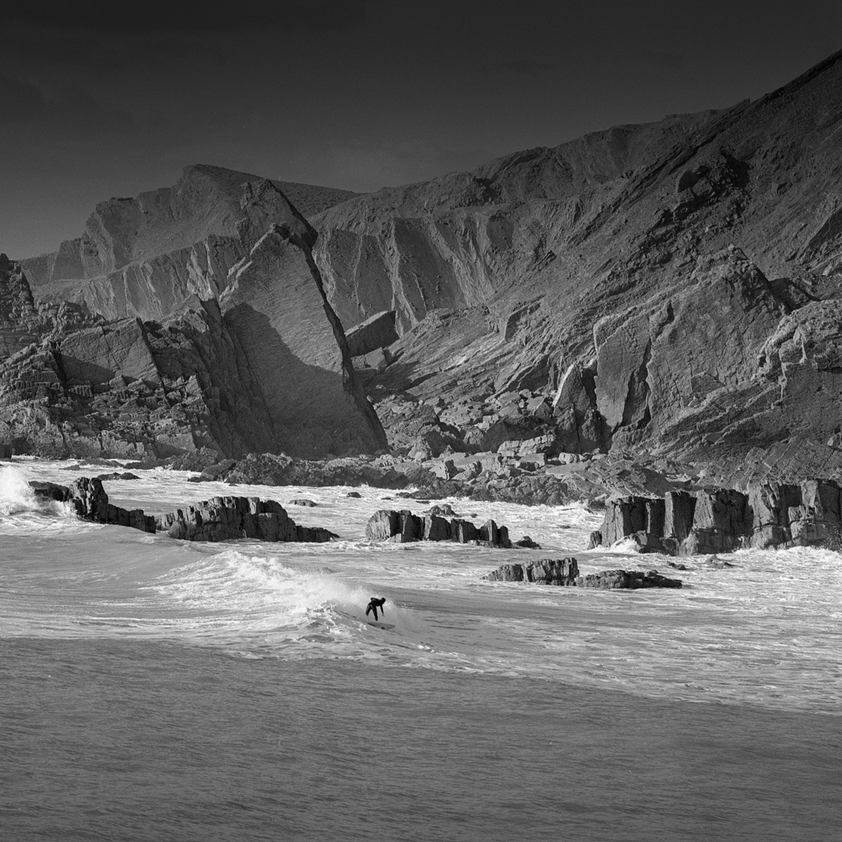 Surfing in the ocean with large rocks behind