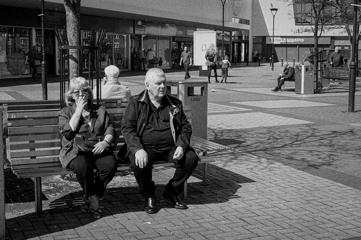 Two people sat down on a bench on the high street
