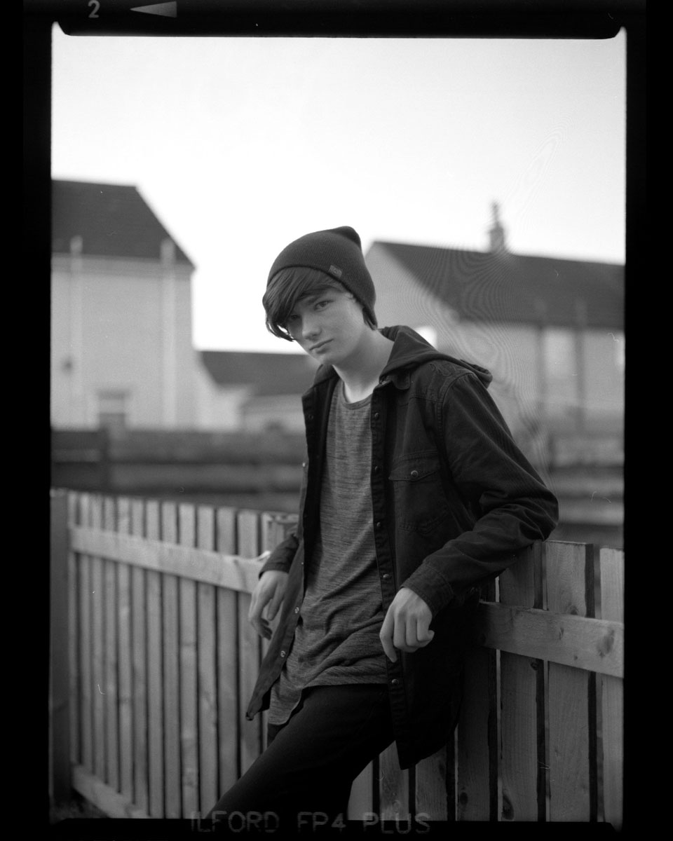 Black and white portrait of a boy stood in front of the fence #ledinglines