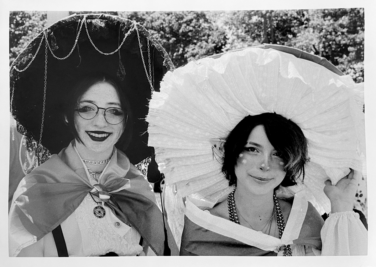 Two ladies with extra large hats on with vibrant make up