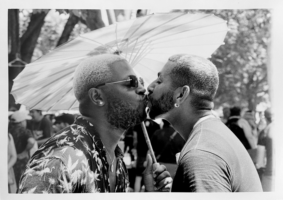 Two men kissing underneath an umbrella