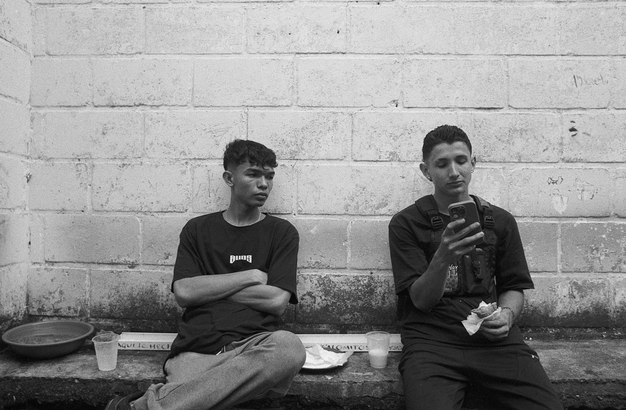 Henry Craver. Black and white shot of two boys sat on a bench talking.