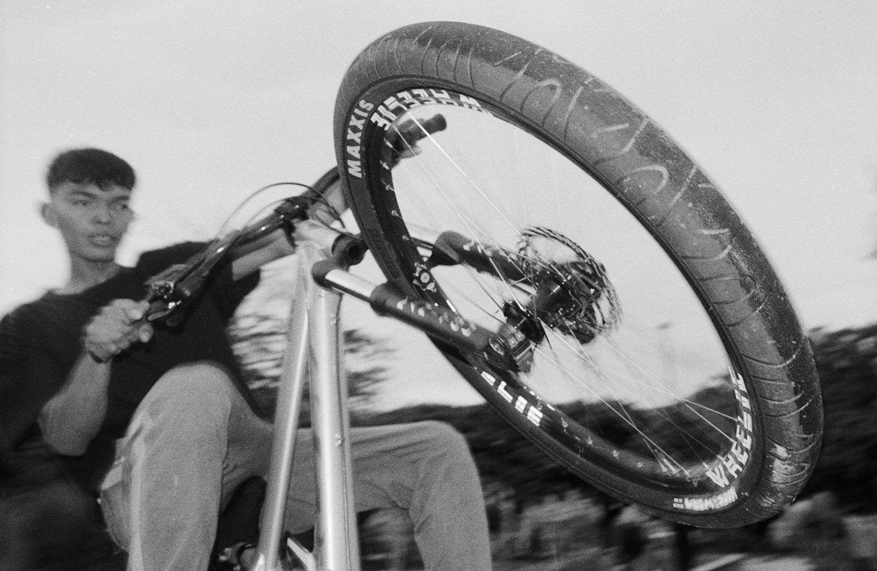 Henry Craver. Black and white shot of a young man doing a wheelie on a bike.
