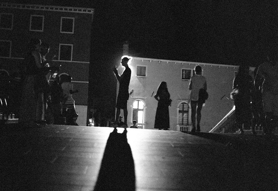 Julian Tanase. Black and white silhouette of people on a bridge at night.