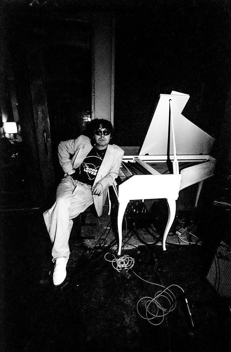 Black and white image of a man in a white suit next to a white piano