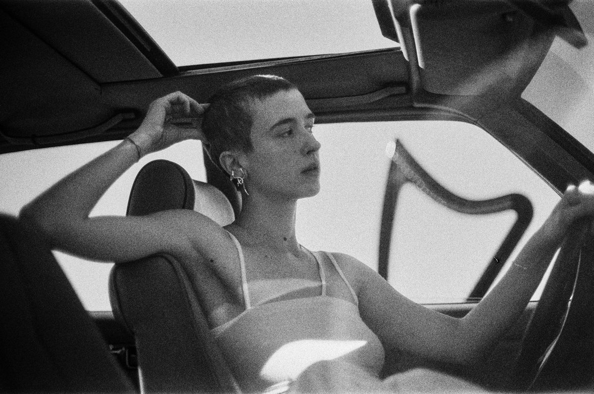 Black and white shot of a woman driving the car with a shaved head