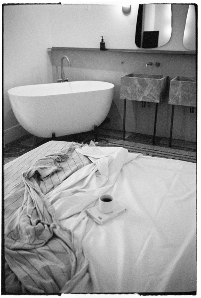 Black and white image of a coffee on a bed with a tub in the background