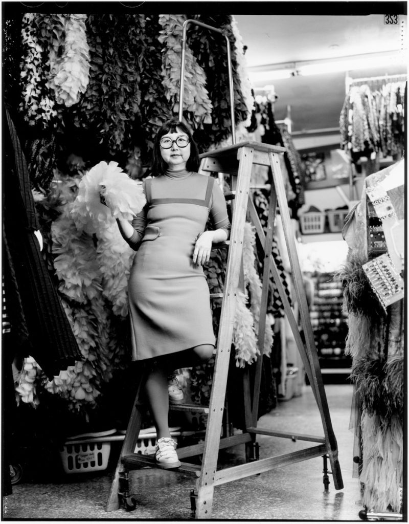 Black and white picture of an Asian woman on a step ladder in a wardrobe