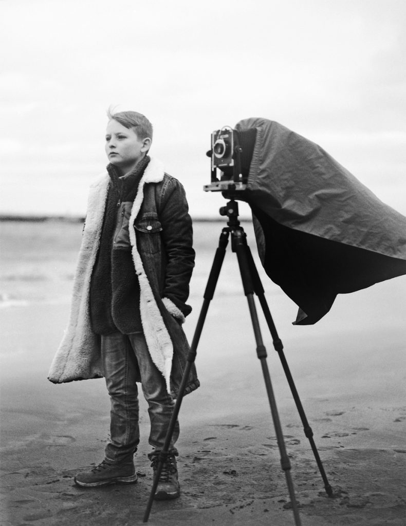 boy stood next to a camera on the beach