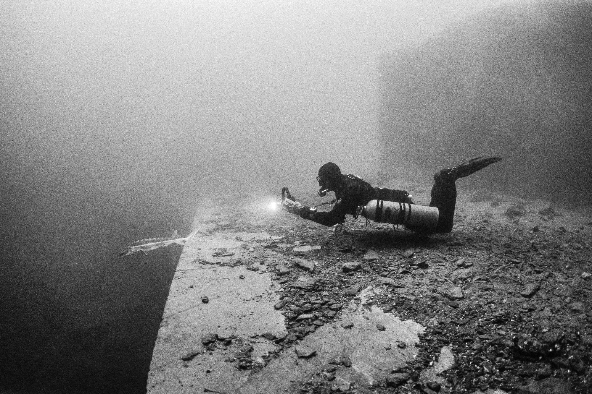 Gilles in side-mount (cave diving setup) chasing a sturgeon — Vodelée, Belgium.Nikonos RS + 13 mm lens, Ilford Delta 400 (pushed 1 stop). 